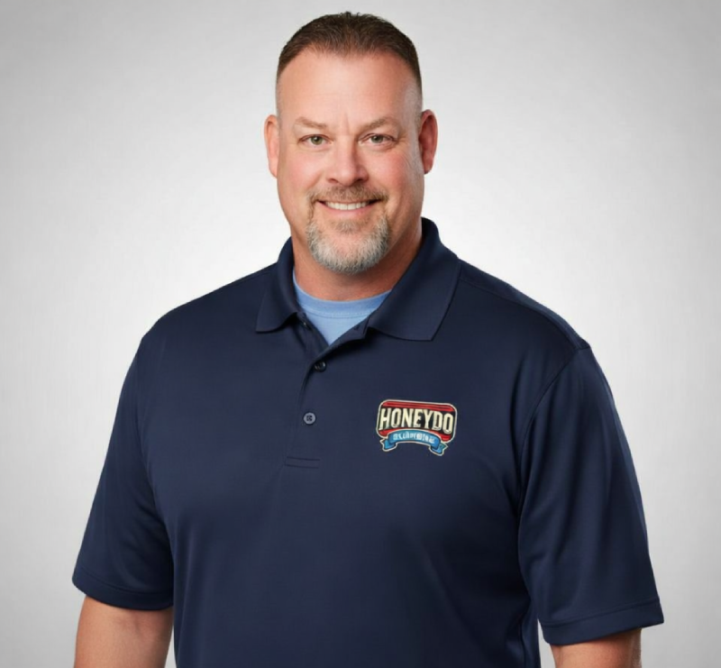 Smiling man in a navy polo shirt with logo against a gray background.