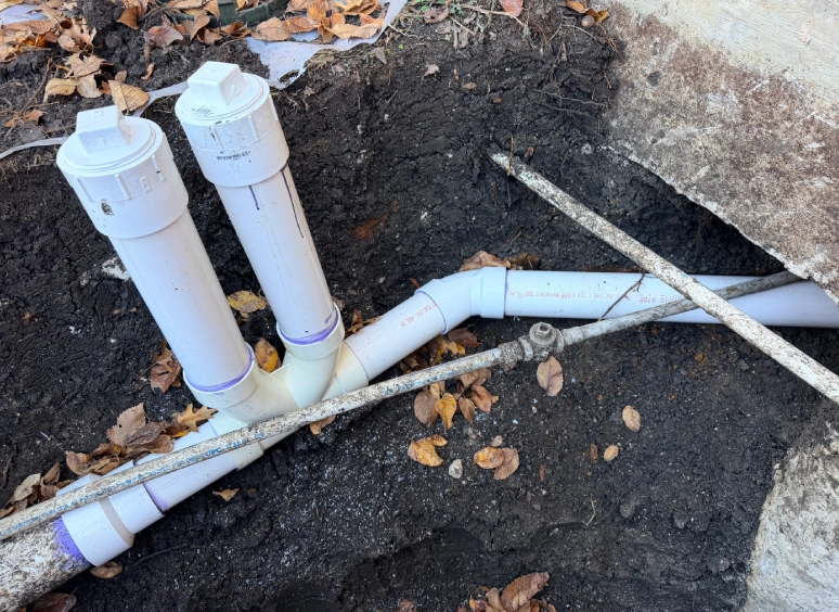 Exposed PVC pipes with elbow joints in a dug-up ground area.