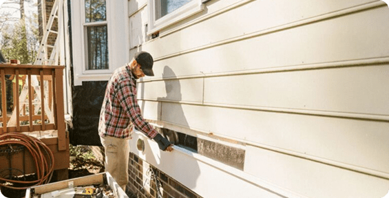 Man installing siding on house exterior.