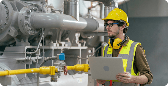 Engineer inspecting machinery with a laptop.