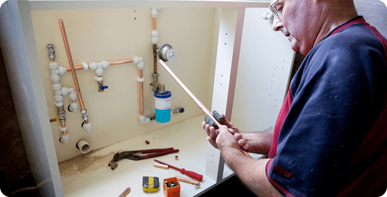 Plumber working under kitchen sink pipes.