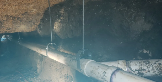 Old rusty water pipe with hanging wires in a dim underground space.
