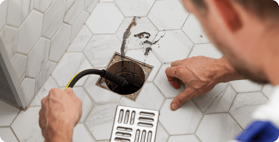 A person cleaning a floor drain.