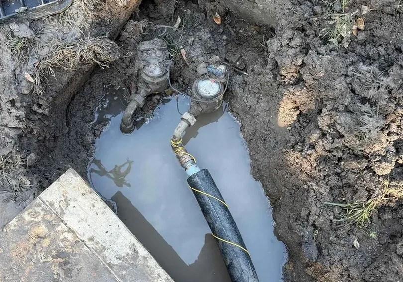 Exposed underground water pipes surrounded by mud and water.