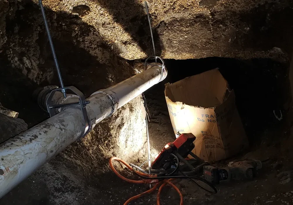 Excavation site with a large pipe and cables underground.