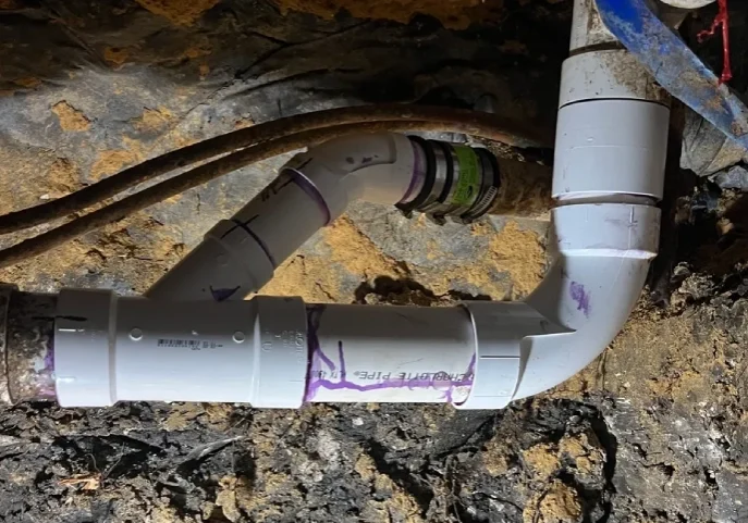 PVC pipe joint with a marked label in a basement or crawl space.